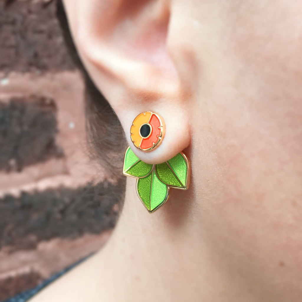 Close up of a person wearing Anenome enamel flower studs with leaf jacket earrings.
