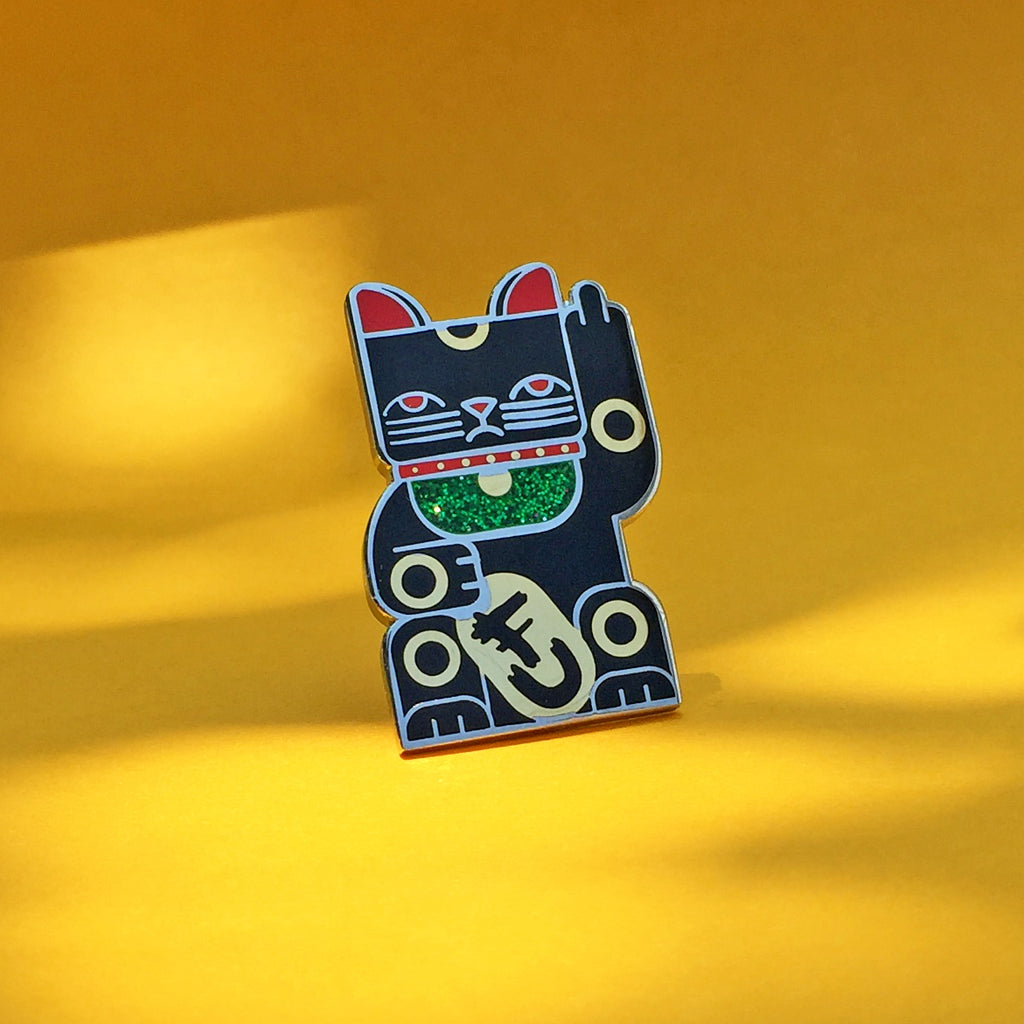 Goodbye Kitty black enamel pin finished in gold and silver with green glitter bib. Shows a maneki neko rudely gesturing.