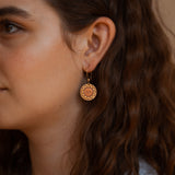 A person wearing Helios solar earrings finished in 24k gold and antique copper.