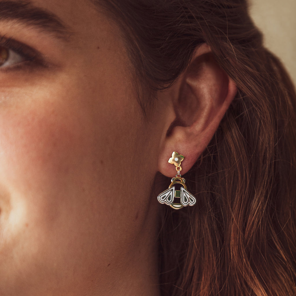 A person wearing Mellona enamel honeybee pendant earrings with gold flower studs.