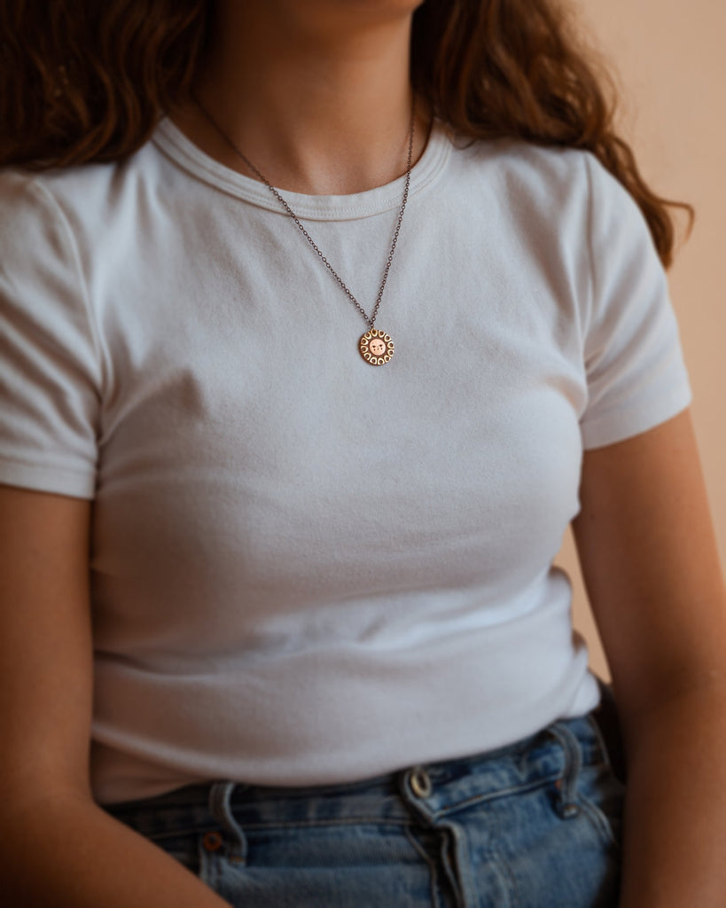 A person wearing Helios solar necklace finished in 24k gold and antique copper. Shows it sitting just below the collar bone.
