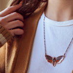 A person wearing an Atropos enamel death's-head moth necklace in copper seconds with black mirrored siofourite crystal skull.