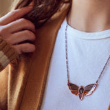 A person wearing an Atropos enamel death's-head moth necklace in copper seconds with black mirrored siofourite crystal skull.