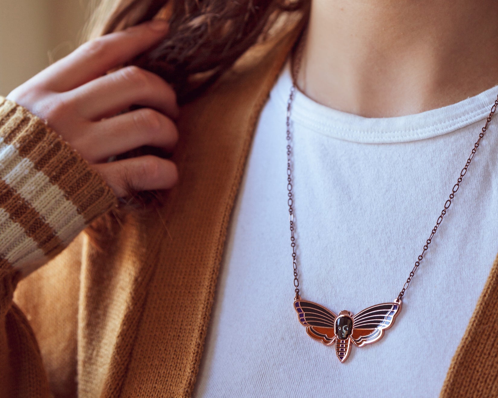 A person wearing an Atropos enamel death's-head moth necklace in copper seconds with black mirrored siofourite crystal skull.
