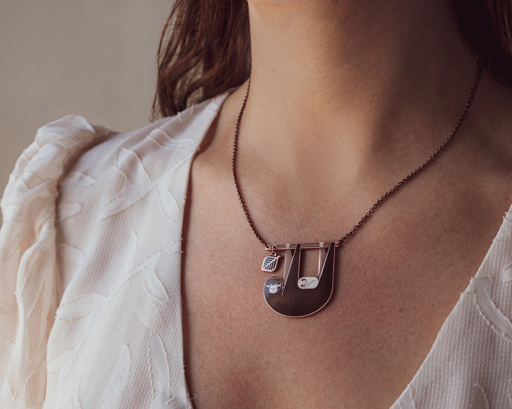 A person wearing Slothlorien sloth and cub necklace, showing how it sits near the collar bone.