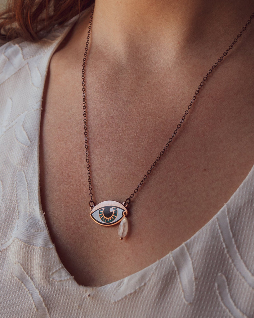 A person wearing an Ersa jade blue enamel eye necklace showing the length sitting at the collarbone.