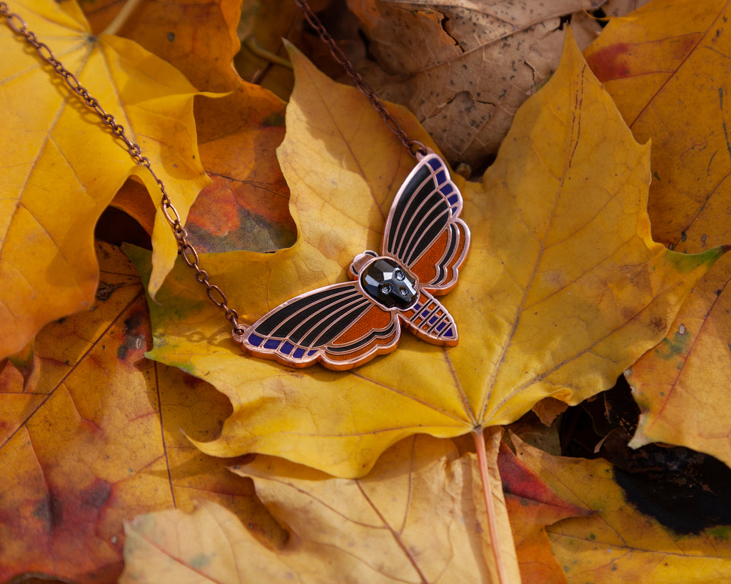 Atropos enamel death's-head moth necklace in copper with black mirrored siofourite crystal skull among autumn leaves.