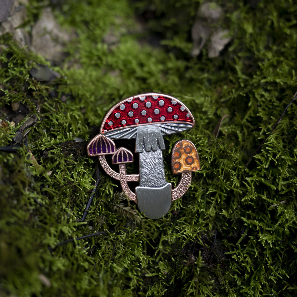 Mycelia mushroom pin in antique copper and silver, laying on green moss. With translucent red, purple and orange enamel.