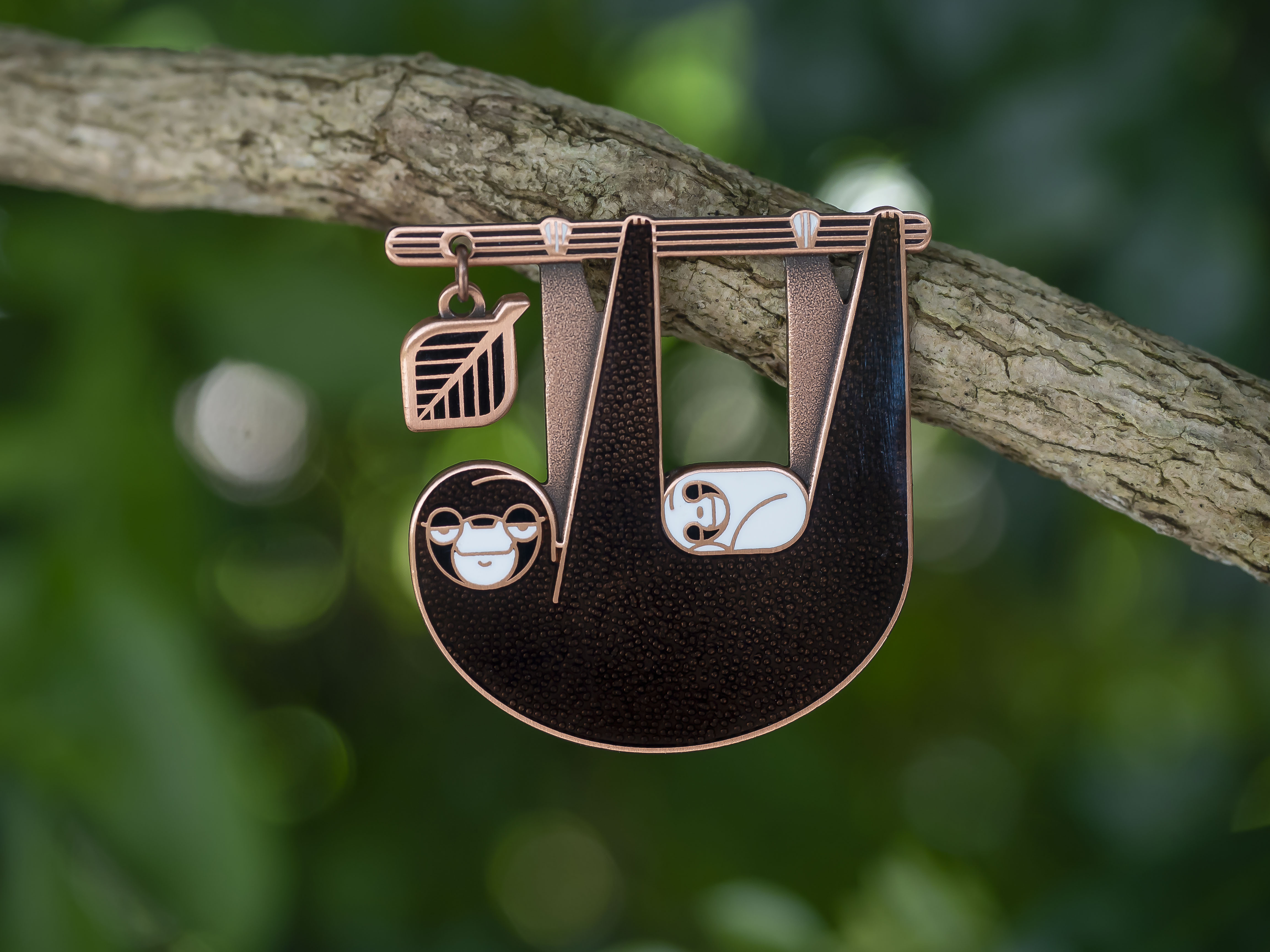 Slothlorien sloth and sleeping cub enamel pin seconds in antique copper. Black enamel, with white cub and leaf dangle.