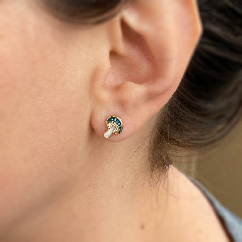 Close up of a person wearing an emerald enamel Amanita mushroom earring stud.