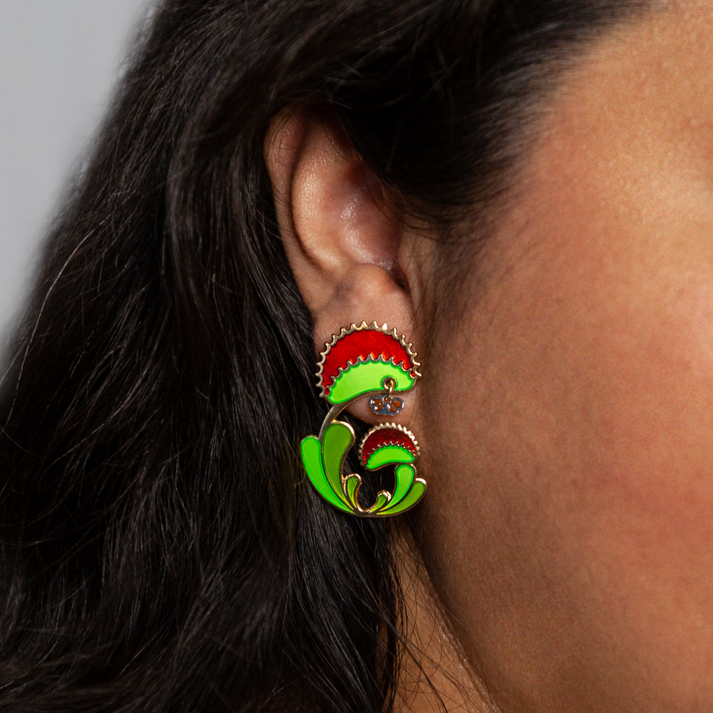 A person wearing a Venus Flytrap earring seconds. Shows the mouth of the plant on the lobe, with the fly dangle just beneath.