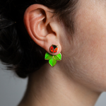 A person wearing Coccinella enamel ladybug or ladybird stud and leaf jacket earrings.