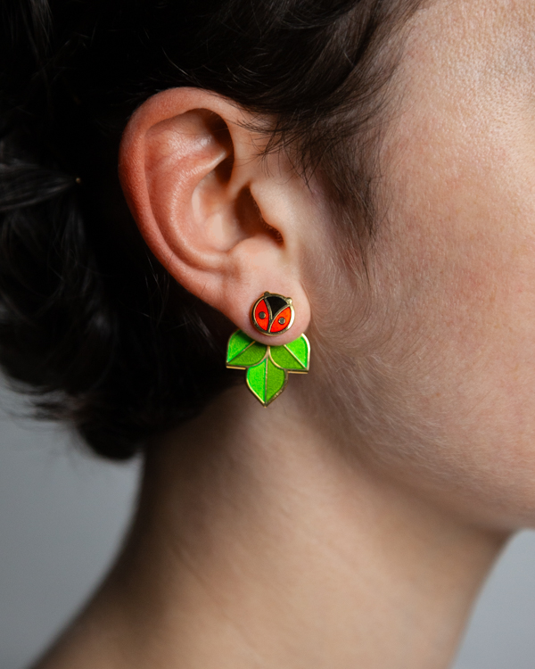 A person wearing Coccinella enamel ladybug or ladybird stud and leaf jacket earrings.