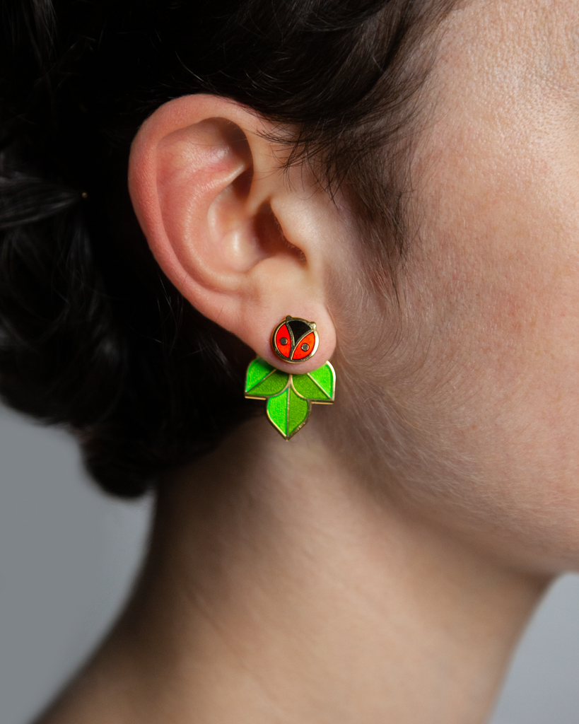 A person wearing Coccinella enamel ladybug or ladybird stud and leaf jacket earrings.