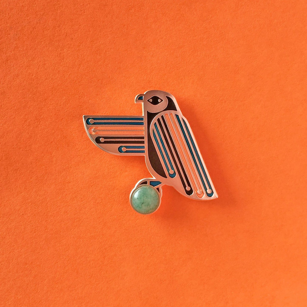 Apollos enamel hawk pin with green aventurine cabochon and blue, black and orange stripes.