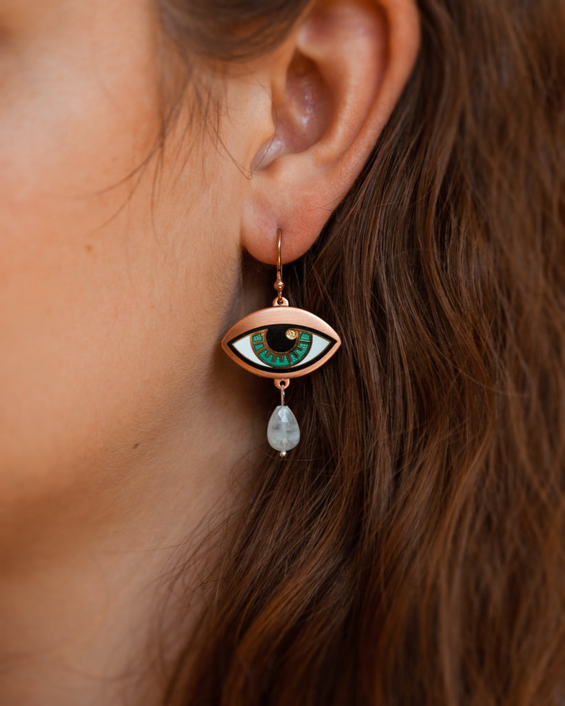 A person wearing a jade blue Ersa eye earring seconds in gold and antique copper with a rainbow moonstone teardrop.