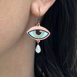 A person wearing a jade blue Ersa eye earring seconds in gold and antique copper with a rainbow moonstone teardrop.