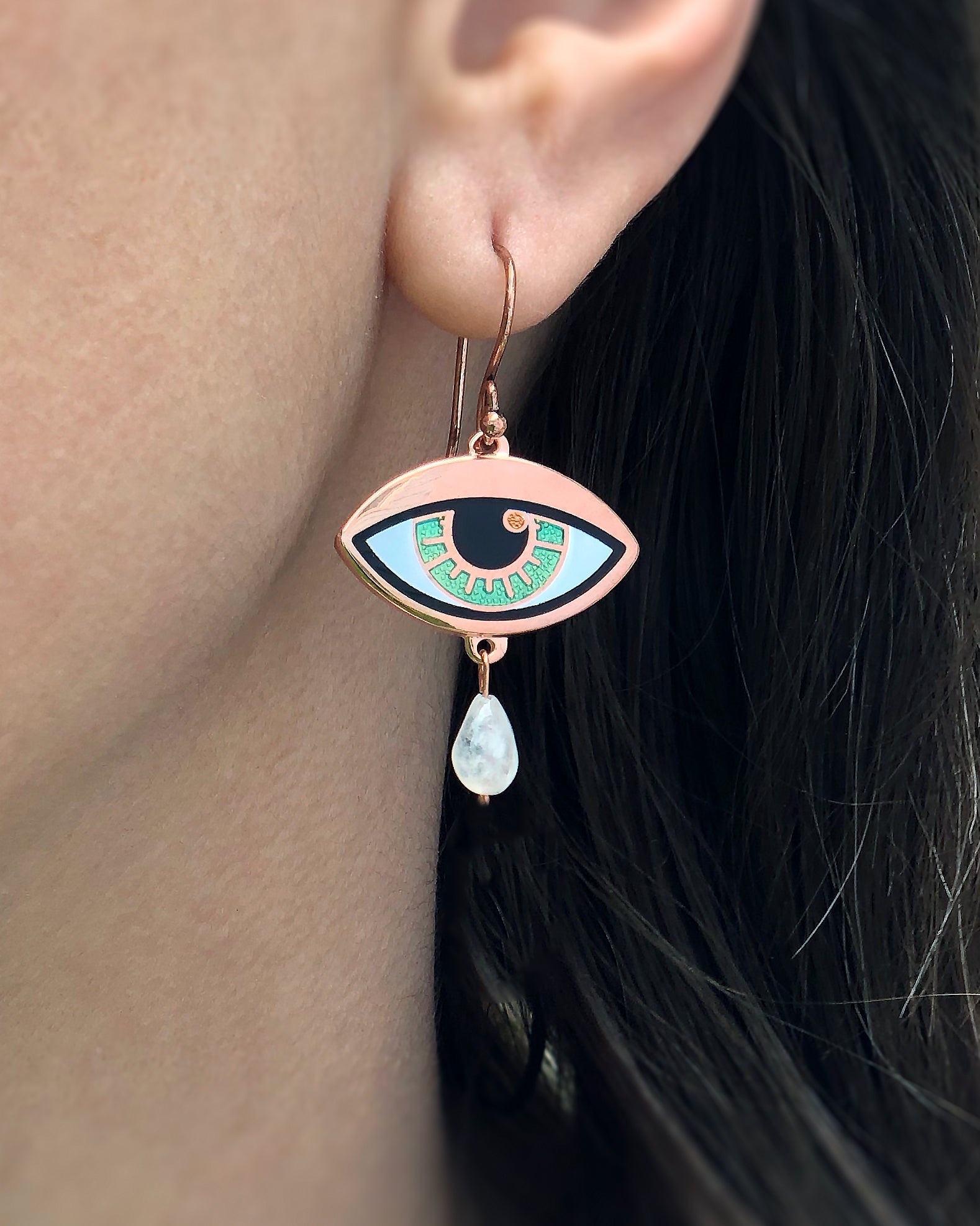 A person wearing a jade blue Ersa eye earring seconds in gold and antique copper with a rainbow moonstone teardrop.