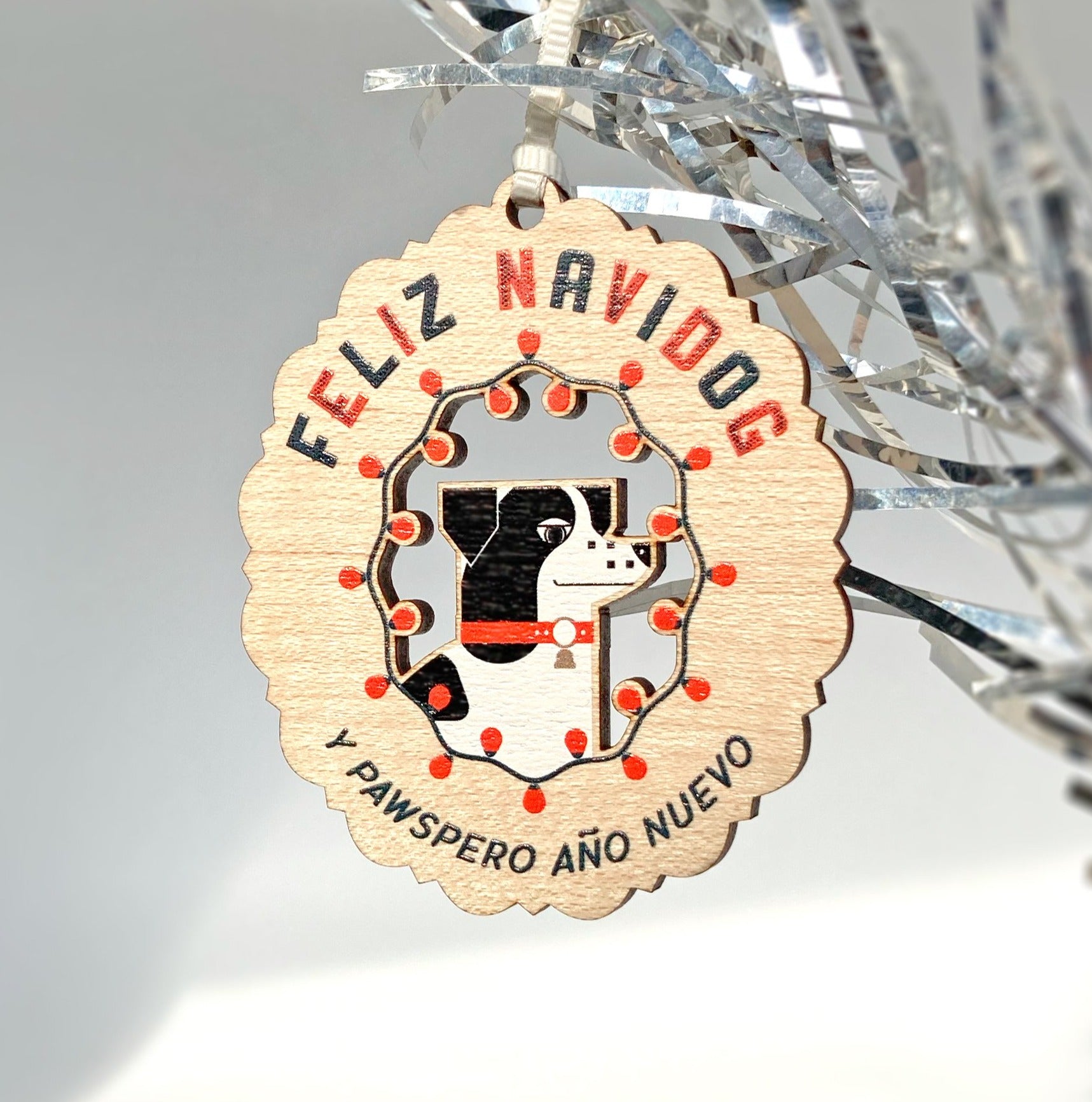 Laser woodcut Feliz Navidog holiday ornament showing a dog surrounded by festive lights in red, green and black.