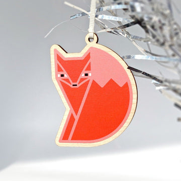 Foxsimile laser woodcut holiday fox ornament in orange and black hung from an aluminum tinsel tree.