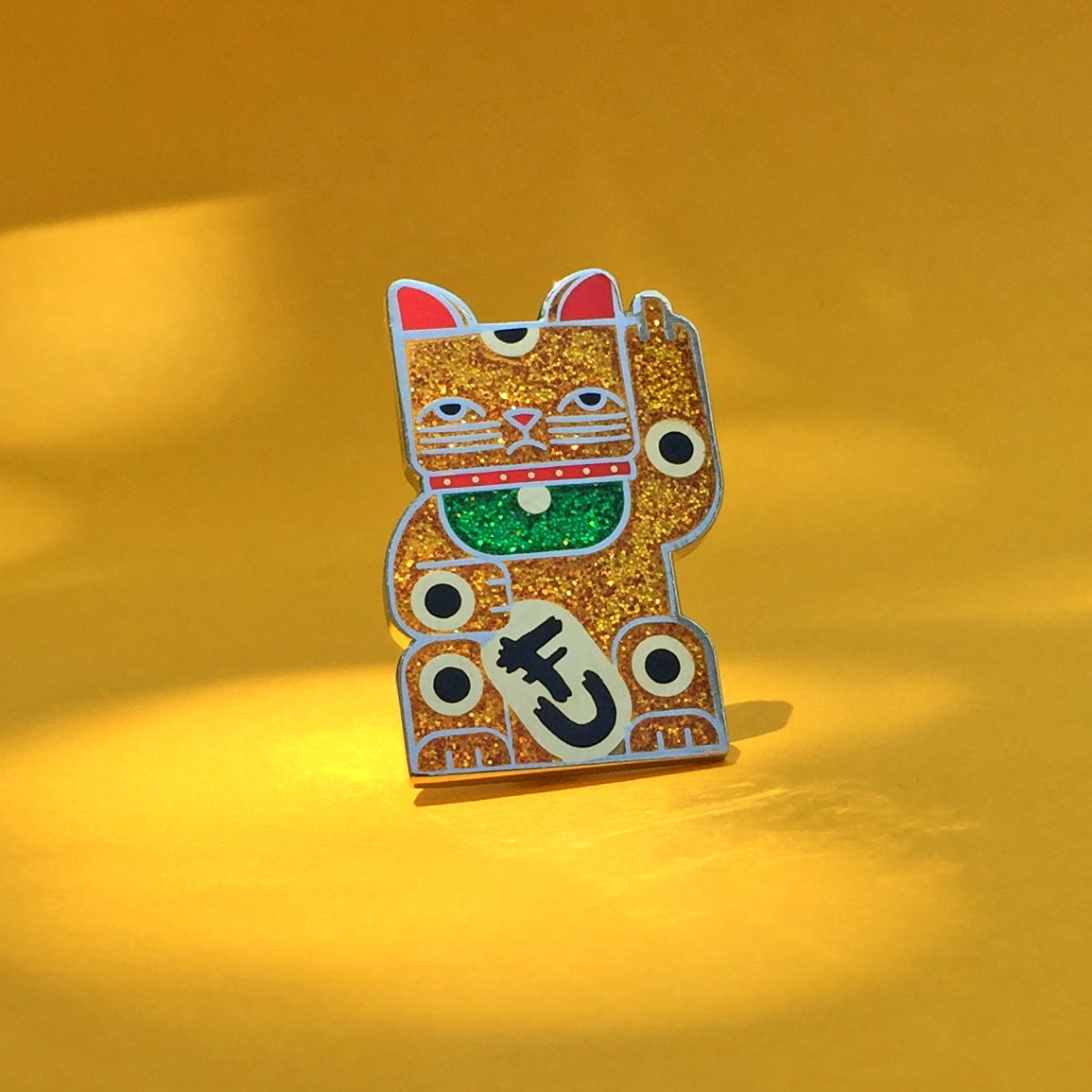 Goodbye Kitty gold glitter enamel pin seconds in gold and silver with green glitter bib. A maneki neko rudely gesturing.