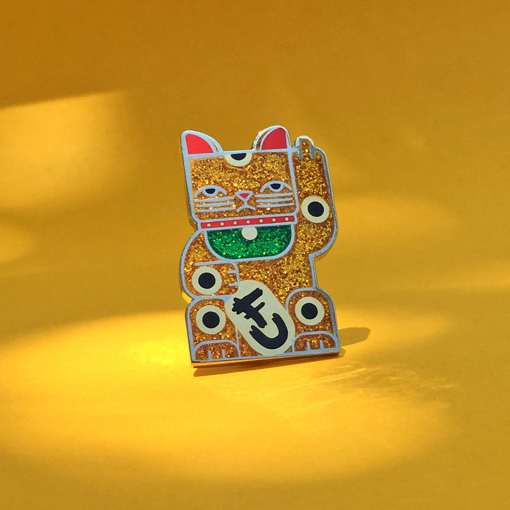 Goodbye Kitty gold glitter enamel pin seconds in gold and silver with green glitter bib. A maneki neko rudely gesturing.
