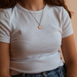 A person wearing Helios solar necklace finished in 24k gold and antique copper. Shows it sitting just below the collar bone.