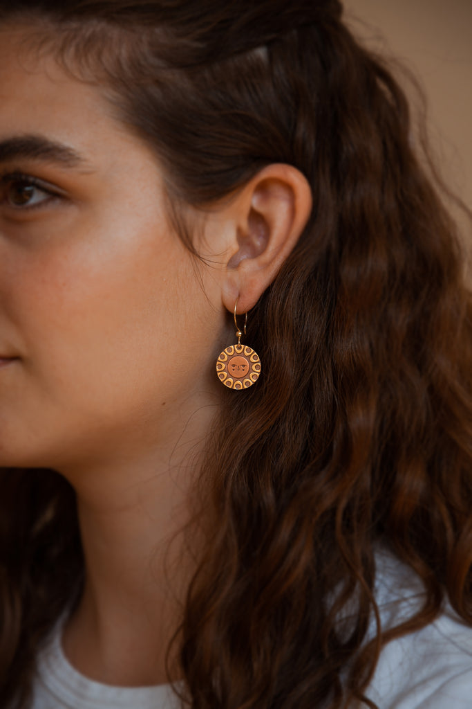 A person wearing Helios solar earrings finished in 24k gold and antique copper.