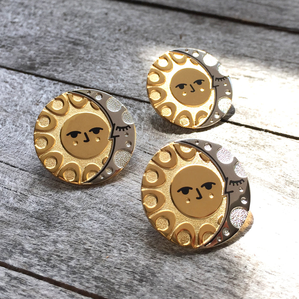 A group of Illumine solar and lunar enamel pins in gold and silver. With a classic sun face and sleeping moon.