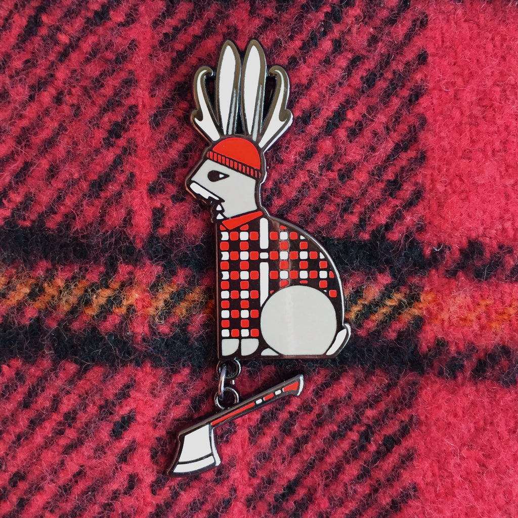 Lumberjackalope enamel pin in red, black, grey and white. Lumberjack jackalope with an axe dangle shown on a plaid shirt.