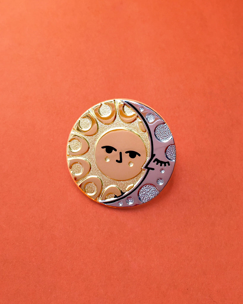 Illumine solar and lunar enamel pin in gold and silver. With a classic sun face and sleeping moon.