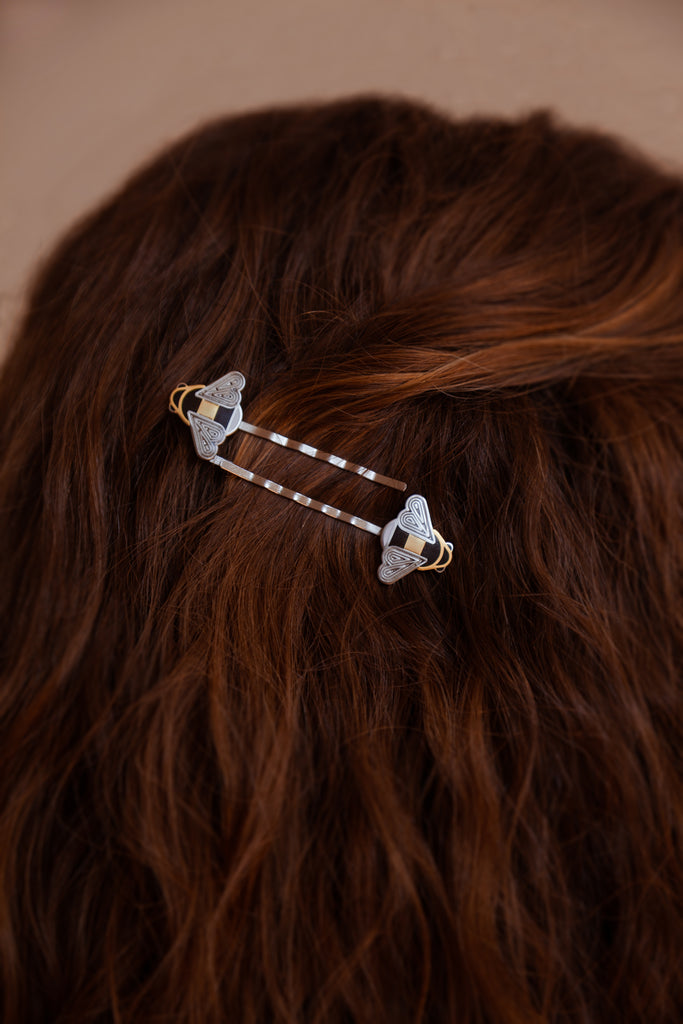 A person wearing a pair of Mellona black and white enamel honeybee hairpins in gold and silver.