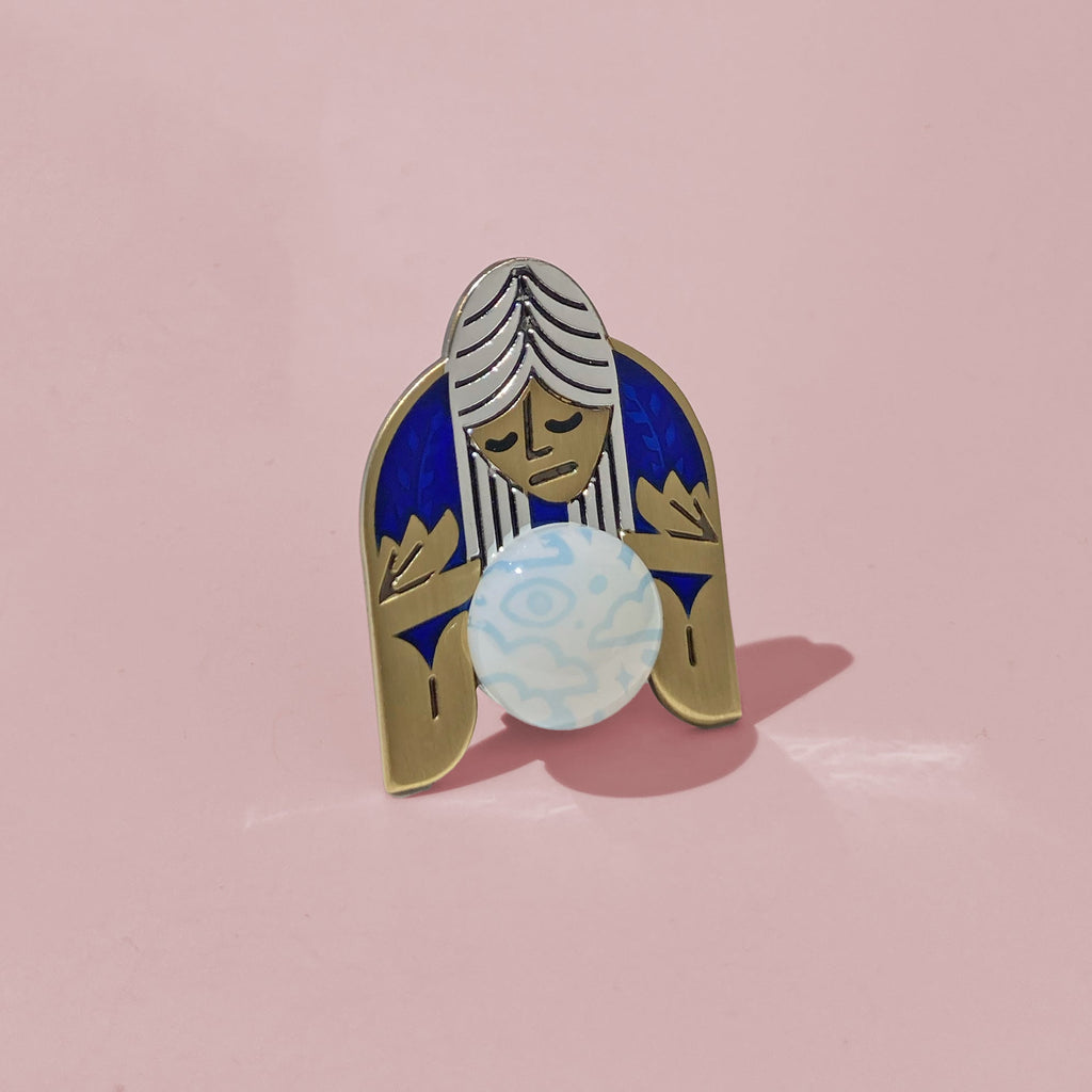 Oracle blue enamel pin in silver and antique bronze. Shows a psychic mystic peering into a sea opal cabochon crystal ball.