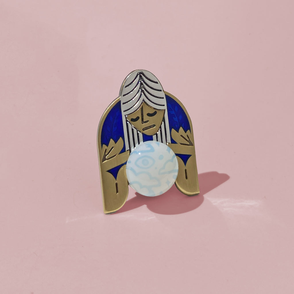 Oracle blue enamel pin in silver and antique bronze. Shows a psychic mystic peering into a sea opal cabochon crystal ball.