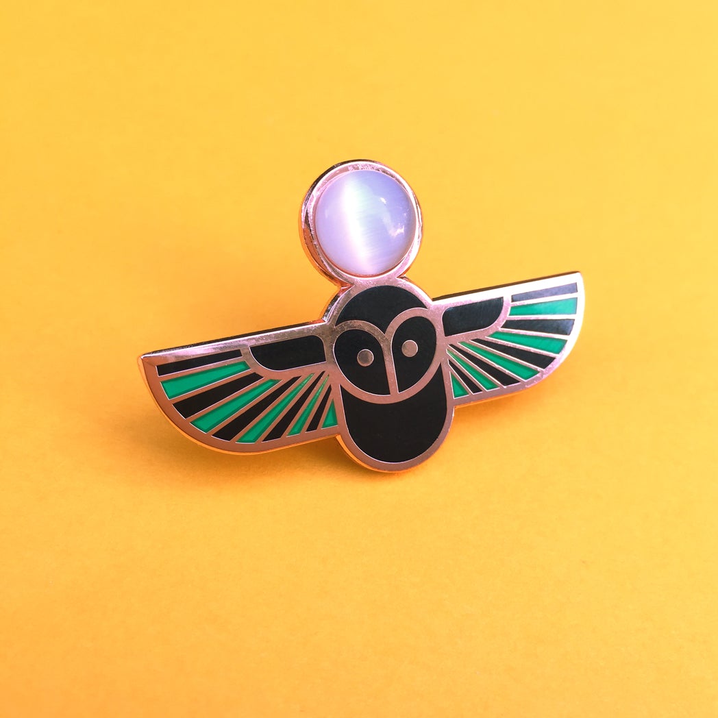 Minerva owl pin seconds in copper with translucent aqua and black enamel set with a white cat's eye cabochon.
