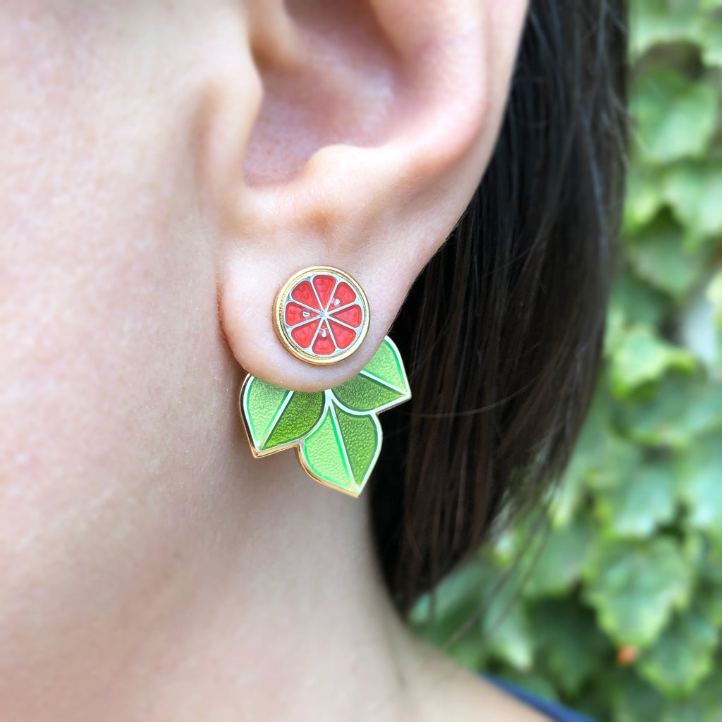 A person wearing a Ruby Red grapefruit earring showing the fruit stud and leaf jacket behind the ear