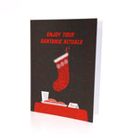 Enjoy Your Santanic Rituals christmas greeting card in black and red. Depicts a stocking, milk and cookies.