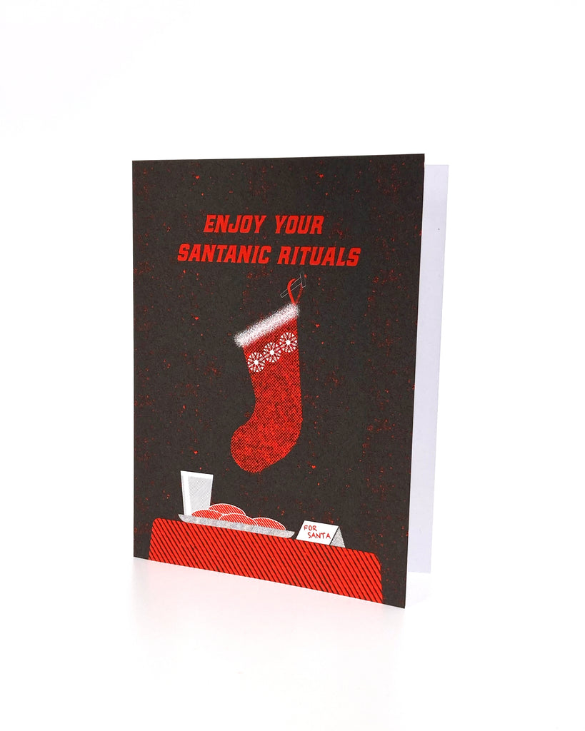 Enjoy Your Santanic Rituals christmas greeting card in black and red. Depicts a stocking, milk and cookies.