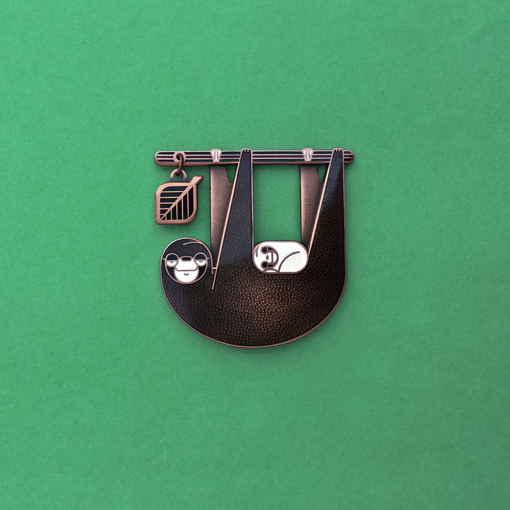 Slothlorien sloth and sleeping cub enamel pin in antique copper. Translucent black enamel, with white cub and leaf dangle.