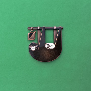 Slothlorien sloth and sleeping cub enamel pin in antique copper. Translucent black enamel, with white cub and leaf dangle.